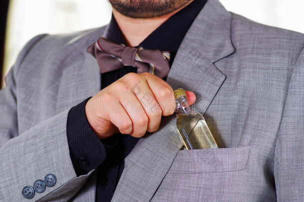特写男子的胸部区域穿着正式的西装和领带，把小酒瓶放在夹克口袋里，男人穿好衣服