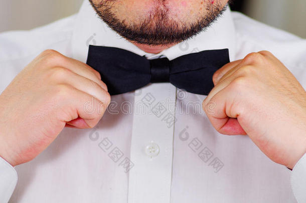 特写男人的胸部穿着白色衬衫，用手系蝴蝶结，脸部分可见，男人穿衣服的概念