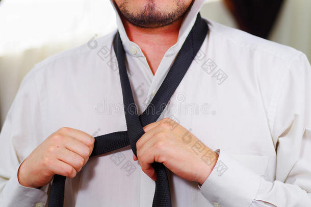 特写<strong>男人</strong>的胸部穿着白色衬衫，用手系领带，脸部分可见，<strong>男人穿衣</strong>服的概念