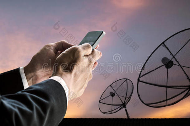 商人使用智能手机，与剪影电信卫星碟数字网络和日落天空
