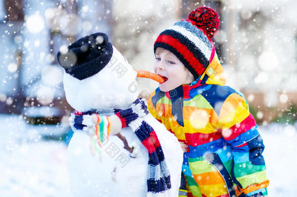 有趣的男孩穿着五颜六色的衣服在户外堆雪人