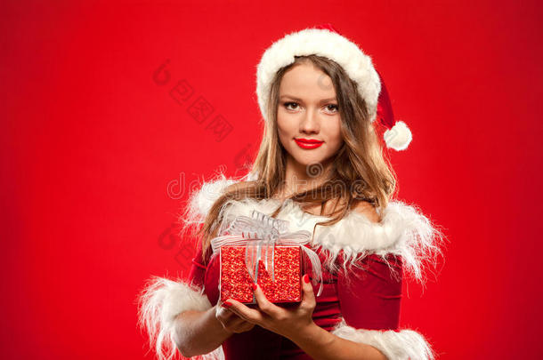圣诞节，圣诞节，冬天，幸福的概念-微笑的女人戴着圣诞老人的帽子，带着礼品盒，红色背景