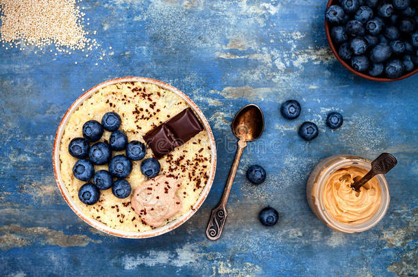 无麸质苋菜和藜麦粥早餐碗与蓝莓和巧克力在乡村木制背景。