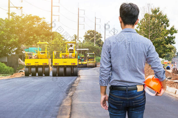 工程师在道路施工现场戴安全帽，用压路机工作沥青道路