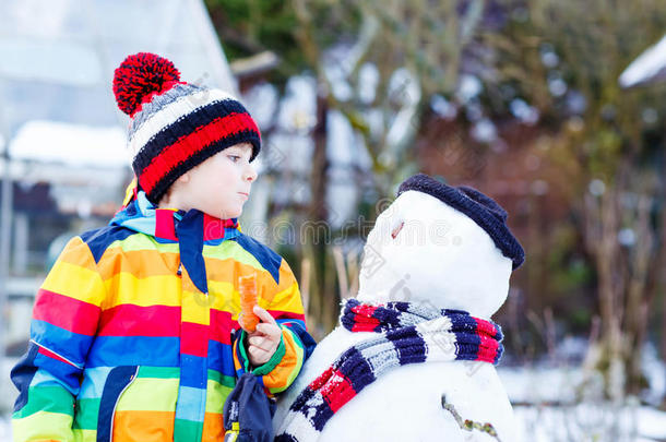 有趣的男孩穿着五颜六色的衣服在户外堆雪人