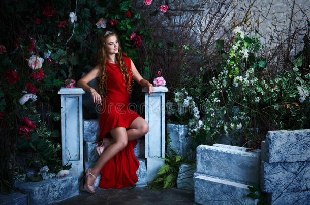 童话故事。 穿着红色连衣裙的美丽公主坐在一个神秘的花园里