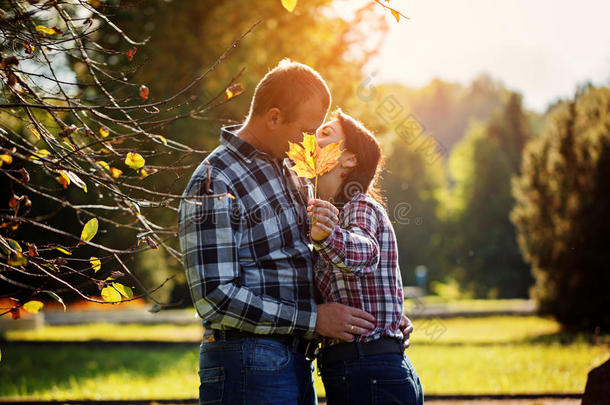 秋天户外可爱的一对。 年轻的男人和女人亲吻隐藏在枫叶后面。