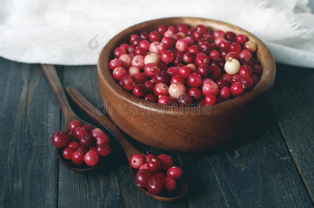 新鲜的红森林蔓越莓在一个圆形的碗里，在桌子表面的白色亚麻布上有一个木勺