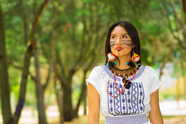 美丽的亚马逊河女人，脸上涂着当地人的颜料，穿着白色的传统服装，在公园里愉快地摆<strong>姿势拍照</strong>