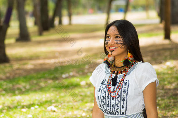 美丽的亚马逊河女人，脸上涂着当地人的颜料，穿着白色的传统服装，在公园里愉快地摆<strong>姿势拍照</strong>