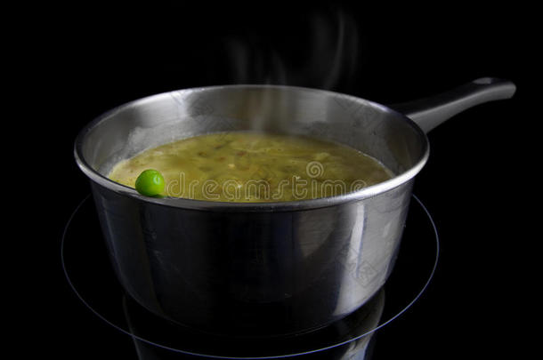 新鲜的豌豆在一个锅与蒸蔬菜汤在感应加热器，黑色背景，概念的维生素保护公司