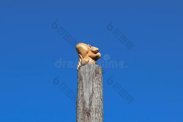 在蓝天的背景上，树桩上有一颗坚果的小松鼠雕像。 用木头做的动物的数字。 木雕