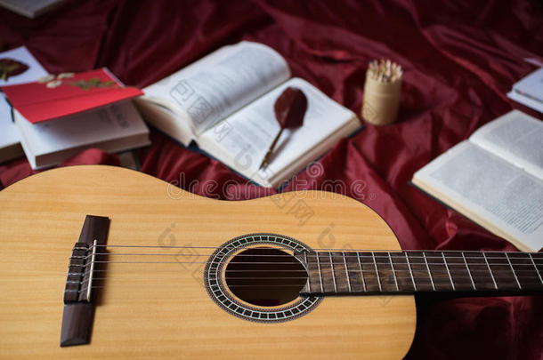 吉他躺在红色的布料上，干花，红色背景上的书