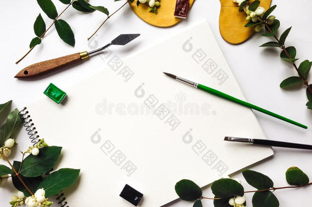 秋天的构图，有相册，水彩画和画笔，装饰着绿色的雪莓树枝和浆果。 平躺，俯视