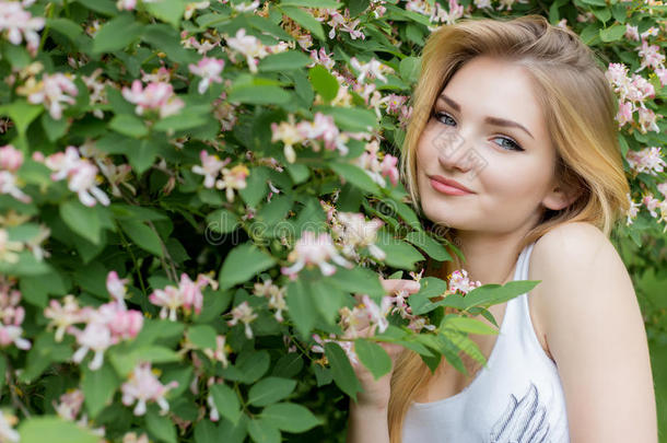 美丽可爱的女孩，留着<strong>长长</strong>的金发，在盛开的玫瑰花丛中享受大自然，穿着一件白色的t恤，嘴唇丰满，夏天明亮