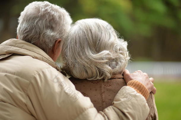 一对年迈的夫妇背对着他的背，拥抱在秋天的公园里