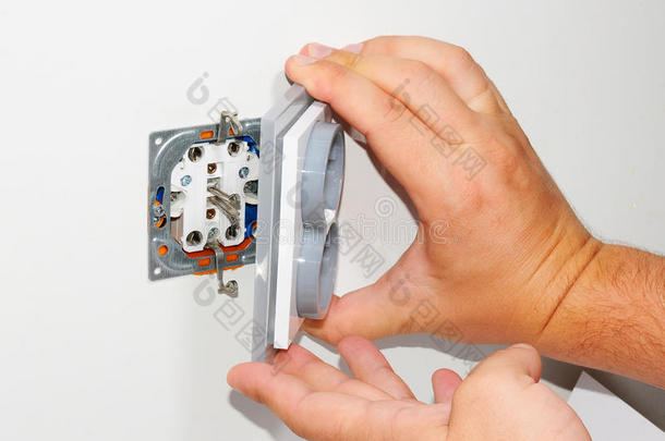 电工在白色<strong>墙上</strong>安装了一个灰色的壁挂式交流电源插座，用螺丝刀在白色<strong>墙上</strong>，翻修了家。