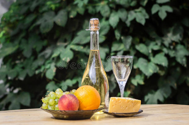 木制圆桌上奶酪、葡萄、桃子、白色、瓶子和眼镜酒的组成。 在院子里。