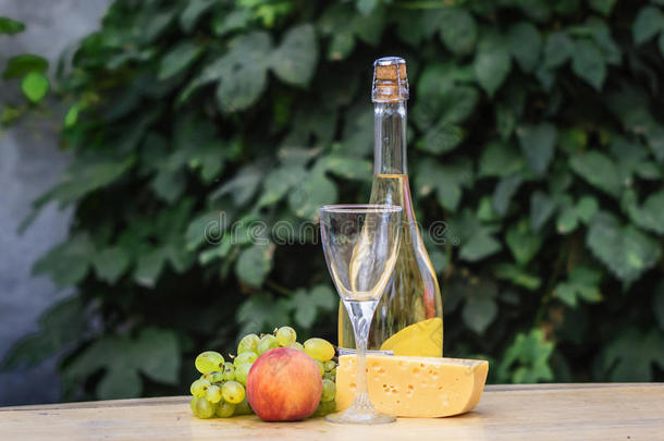 木制<strong>圆桌</strong>上奶酪、葡萄、桃子、白色、瓶子和眼镜酒的组成。 在院子里。