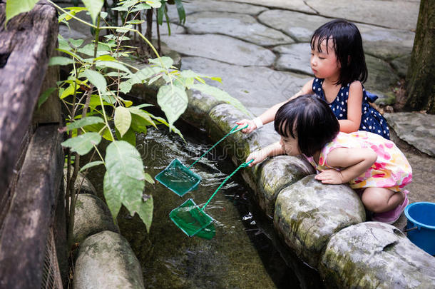 亚洲中国小女孩在池塘用铲子网捕鱼