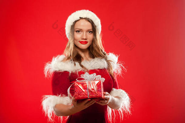 圣诞节，圣诞节，冬天，幸福的概念-微笑的女人戴着圣诞老人的帽子，带着礼品盒，红色背景