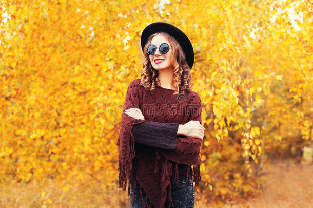 秋季<strong>时尚写真</strong>微笑女士戴着黑帽子墨镜，在阳光明媚的黄叶上编织雨披