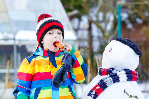有趣的男孩穿着五颜六色的衣服在户外堆雪人
