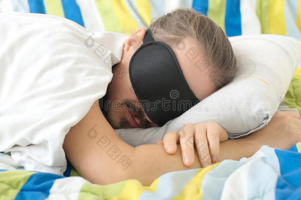 长胡子的年轻人在床上戴着睡眠面具睡觉