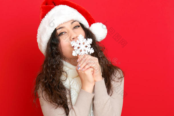 女孩在圣诞帽肖像与大雪花玩具摆在红色背景，圣诞节假期的概念，快乐和情感