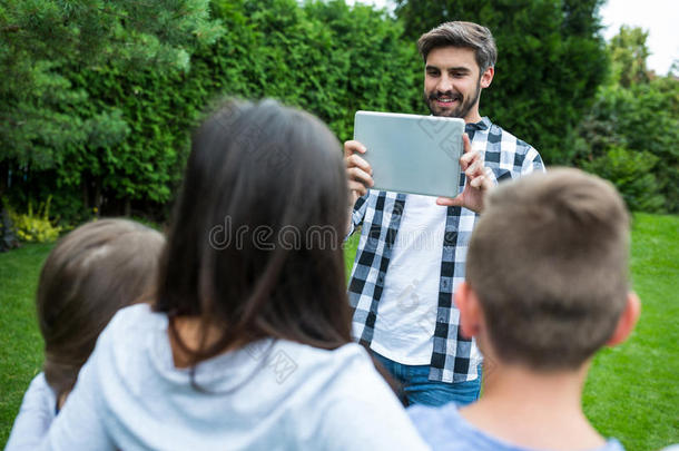 父亲点击图片的家庭从数字平板电脑在公园