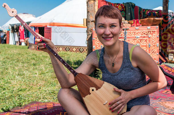 女孩在哈萨克国家乐器演奏-多布拉和坐在蒙古包附近。