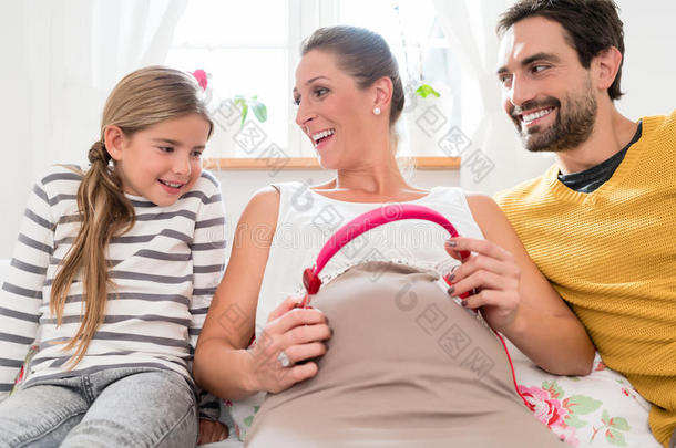 家庭和怀孕妈妈在婴儿肚子上使用耳机