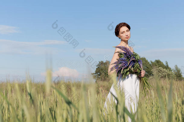 美丽的<strong>甜美</strong>女孩，留着辫子，穿着白色的<strong>夏</strong>季日裙，走在一片田野里，手里拿着一束紫色的卢平花