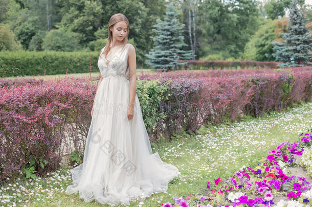 美丽温柔的年轻女子新娘穿着婚纱，温柔的空气走在郁郁葱葱的花园里，在一个炎热的阳光明媚的夏天