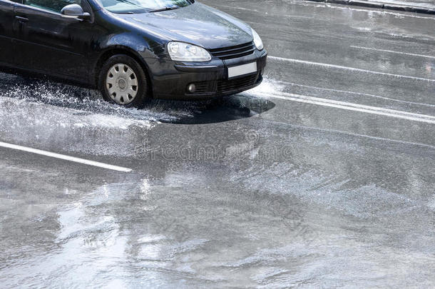 雨后，黑色汽车<strong>驶过</strong>城市街道上的水坑