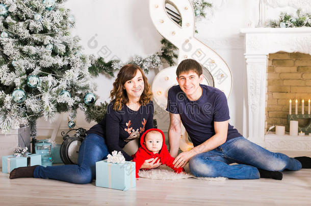 一家人坐在圣诞树下，爸爸妈妈和孩子在装饰好的房间里