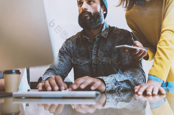 留胡子的人在办公室工作。同事在电脑键盘上打字。 女人站在他<strong>身边</strong>拿着智能手机