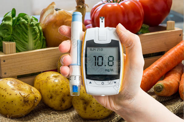 手拿血糖仪测量葡萄糖水平。 背景中的蔬菜。