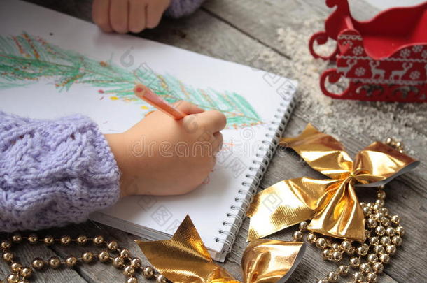 孩子给圣诞老人写信，画一棵圣诞树。 金色圣诞珠和金色丝带蝴蝶结在木制的