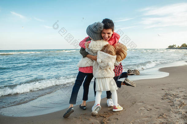 白人白种人家庭的集体肖像，母亲和三个孩子拥抱在夕阳下的海洋海滩上笑着笑