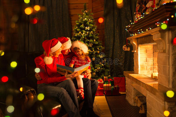 家庭阅<strong>读故事</strong>坐在教练前面的壁炉在圣诞节装饰的房子内部