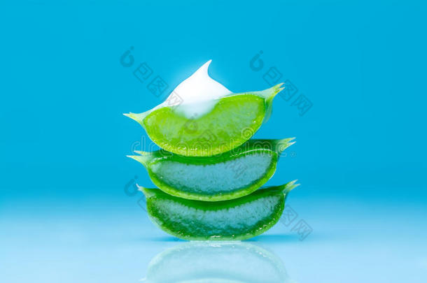 切芦荟叶纹理与一滴美丽的白色奶油与芦荟提取物与反射在蓝色的背景。