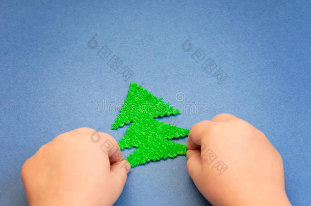 绿色圣诞树在孩子们的<strong>手中</strong>，从<strong>蓝色</strong>纸表面的毛绒材料中剪下