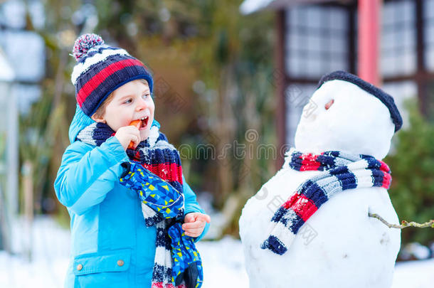 有趣的男孩穿着五颜六色的衣服在户外堆雪人
