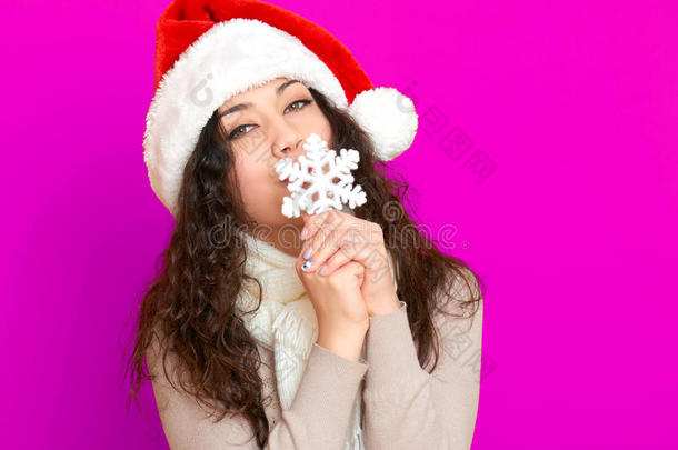 女孩在圣诞帽肖像与大雪花玩具摆在粉红色背景，圣诞节假期的概念，快乐和情感