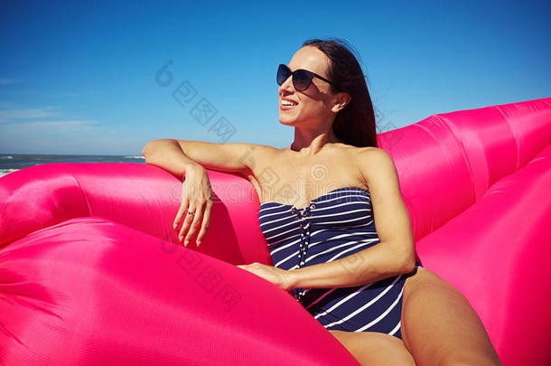 一个可爱的女人坐在海滩上的粉红色<strong>充气船</strong>上