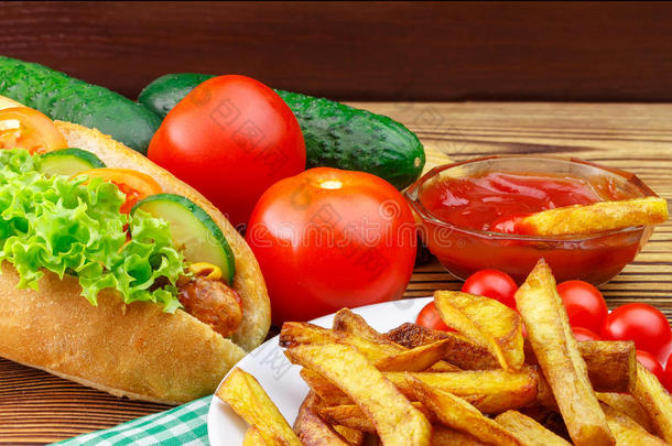 快餐，热狗，炸薯条，番茄酱，番茄和黄瓜在木制背景。