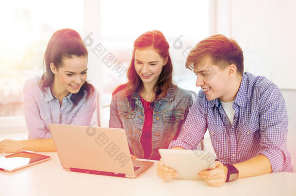 三个面带微笑的学生拿着笔记本电脑和平板电脑