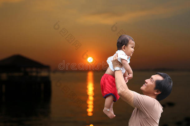 父亲抱着一个婴儿抱着，晚上在泰国海边看日落。