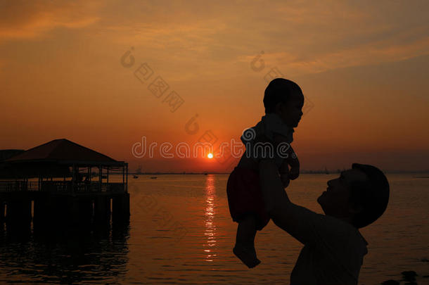 父亲抱着一个婴儿抱着，晚上在泰国海边看日落。